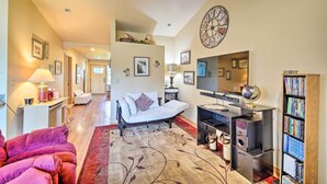 A spacious living room with a sofa, a bed, a bookshelf, and a large clock on the wall. - Upscale Home w/ Indoor Sauna on Sunset Pond! (Ferndale)
