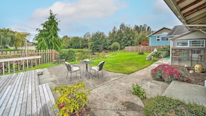 A wooden deck with outdoor furniture, a green lawn, and a greenhouse. - Upscale Home w/ Indoor Sauna on Sunset Pond! (Ferndale)