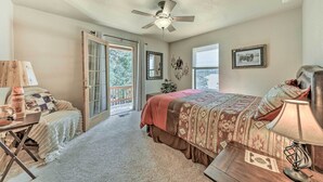 A bedroom with a bed, a desk, a lamp, a ceiling fan, and a sliding glass door leading to a balcony. - Charming Ruidoso Home w/ Deck & Lovely Views! (Ruidoso)