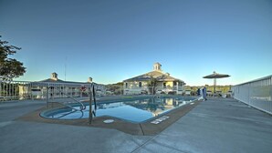 Une piscine entourée d’une clôture, un espace abrité avec un parasol, et un bâtiment avec un toit en forme de dôme en arrière-plan.
