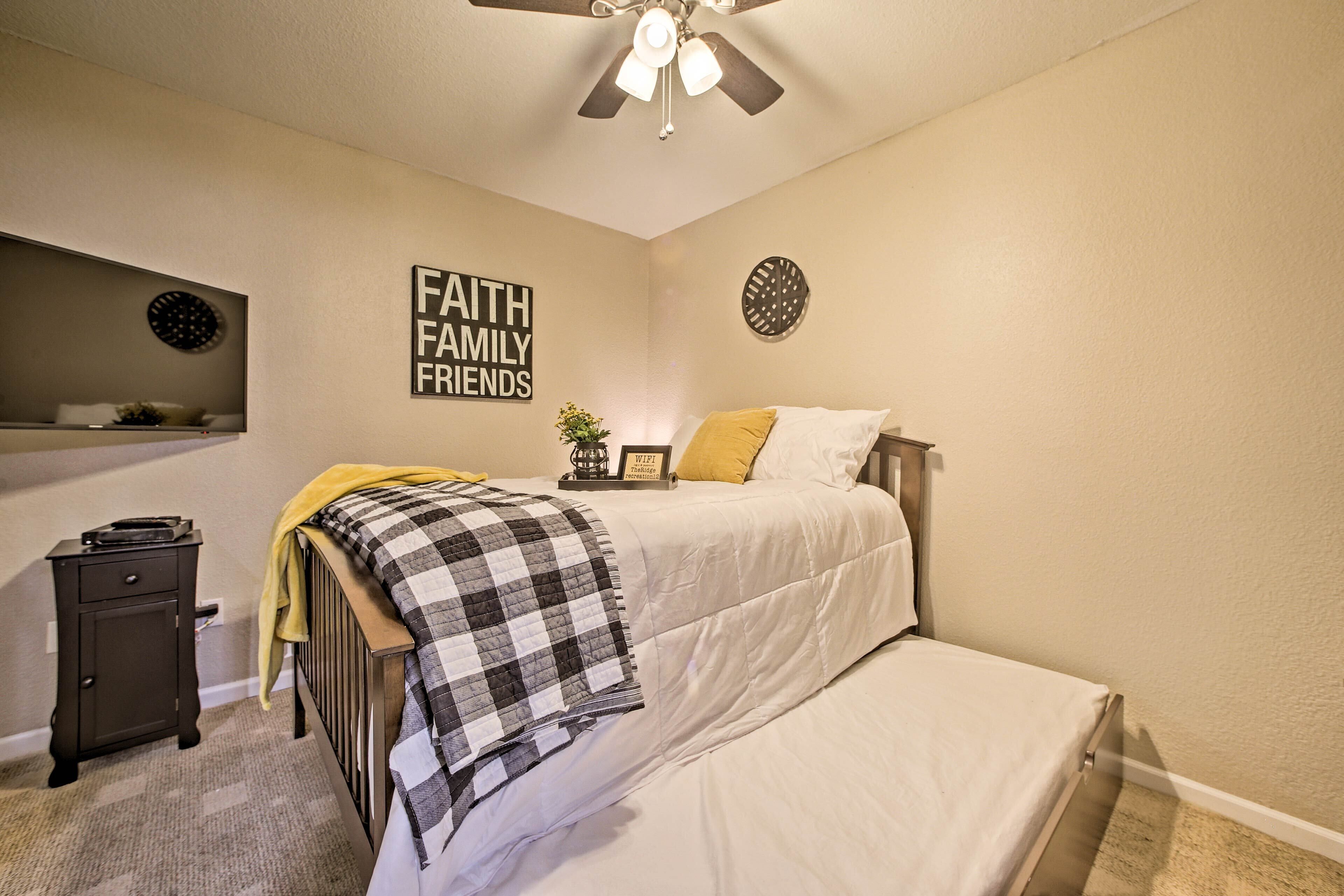 A bedroom with a bed, a nightstand, a ceiling fan, and a wall with a motivational quote.