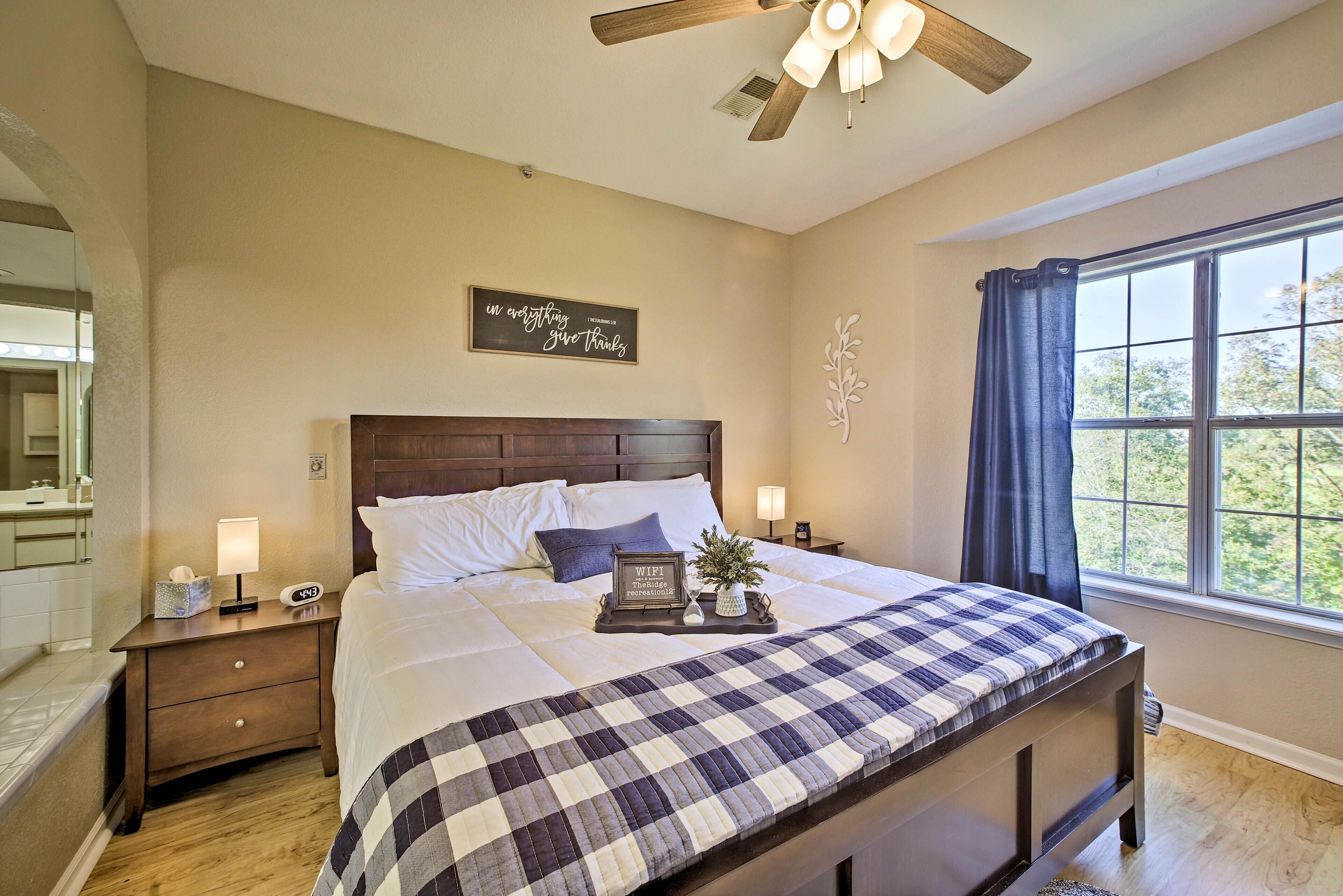 A neatly made bed with a checkered bedspread, a bedside table with a lamp, a clock, and a tray with a plant and a sign.