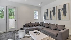 Ein modernes Wohnzimmer mit einem grauen Ecksofa, einem weißen Couchtisch und abstrakter Kunst an der Wand.