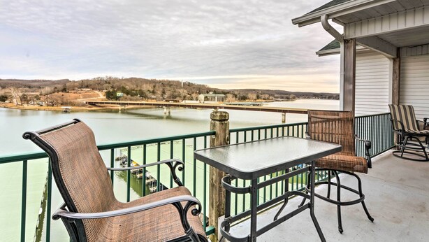 Un balcon avec une table et des chaises donnant sur une étendue d’eau et un paysage lointain.