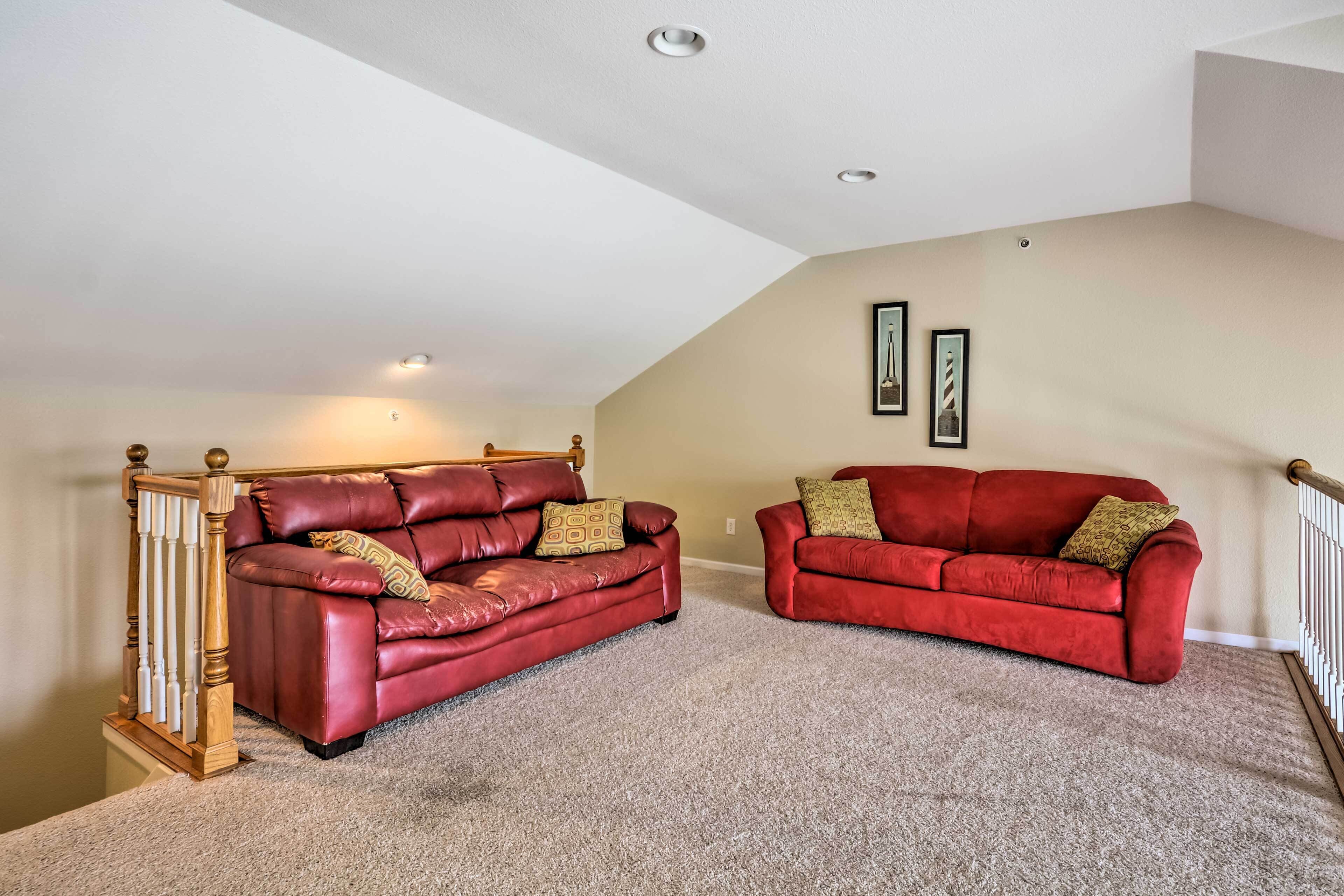 A spacious loft with two red leather sofas, a wooden staircase, and a high ceiling with recessed lighting.