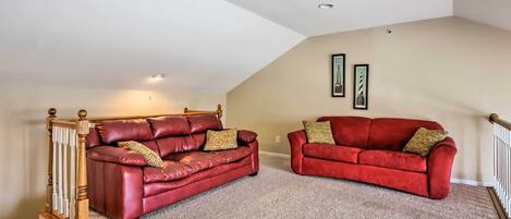 A spacious loft with two red leather sofas, a wooden staircase, and a high ceiling with recessed lighting.