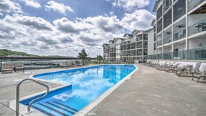 Une piscine équipée d’une rambarde métallique, de chaises longues et d’un immeuble à plusieurs étages doté de balcons.
