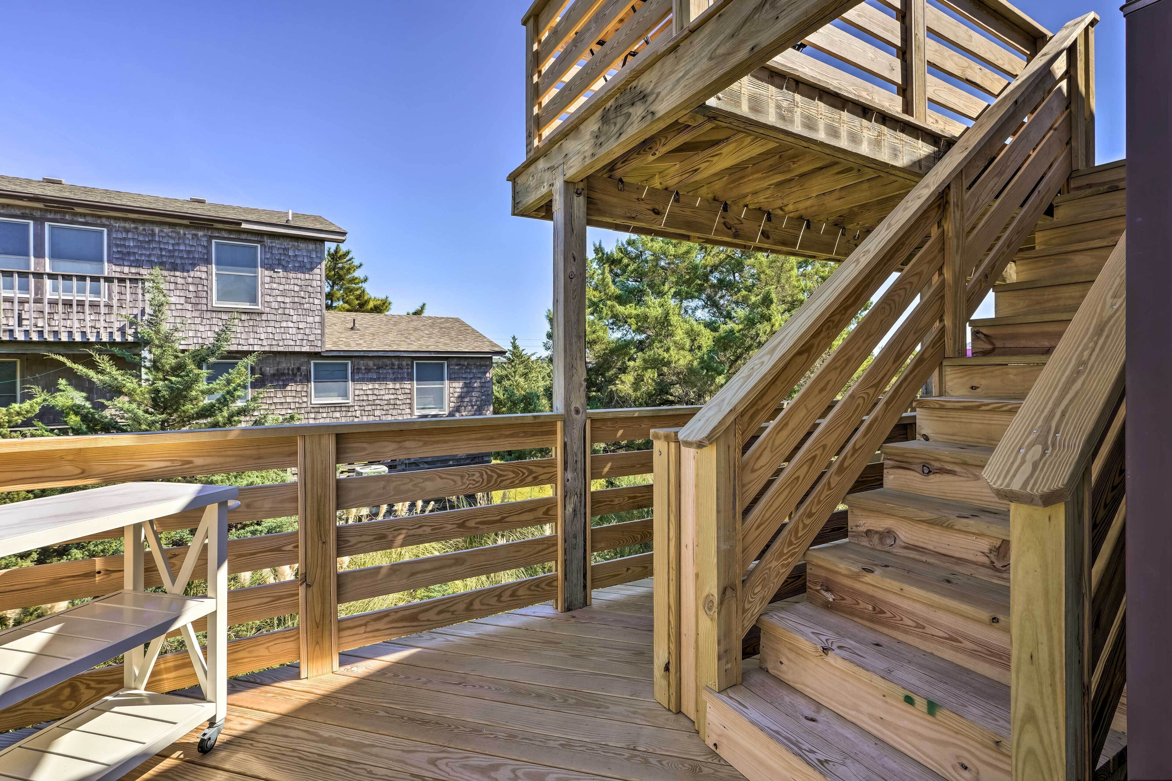 A wooden deck with a staircase leading to a deck level, a table, and a view of a house in the background.