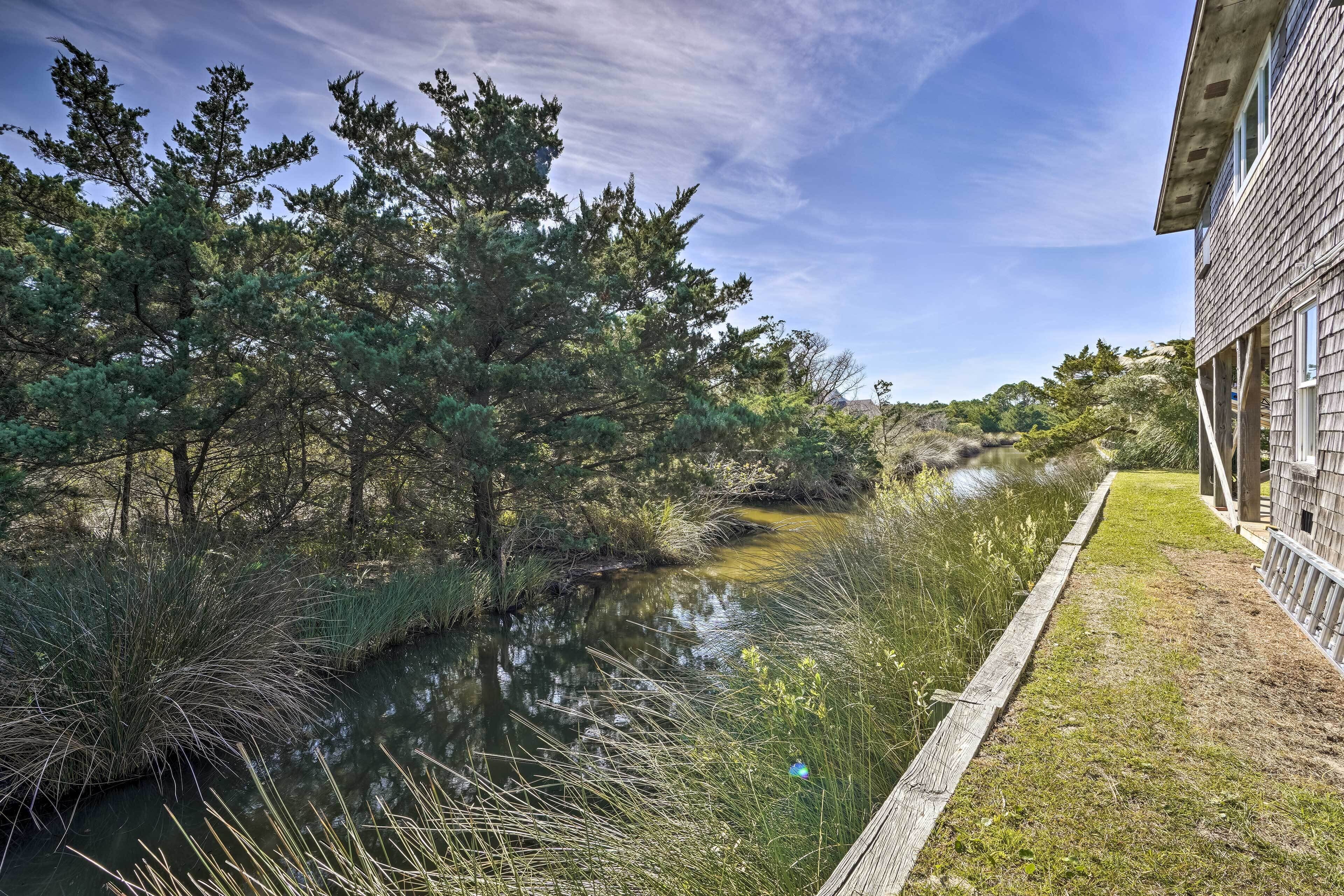 Un sentier qui longe la rivière, agrémenté d’une terrasse en bois, et bordé d’arbres denses et d’une étendue d’eau paisible.