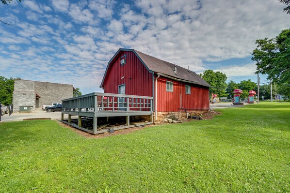 A red barn with a porch, surrounded by green grass and trees. - 12 Mi to Eureka Springs: Charming Studio Retreat (Berryville)