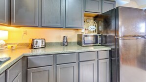 Una cocina con gabinetes grises, un refrigerador de acero inoxidable, un tostador, un microondas y una cafetera.