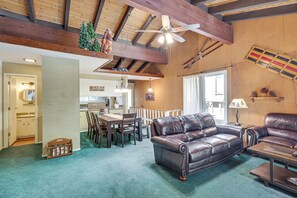 A spacious living area with a leather sofa, dining table, and chairs. A ceiling fan and wooden beams are visible.