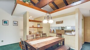 Een eetgedeelte met een houten tafel, stoelen en een bank. Er is een keuken met een aanrecht en kastjes.