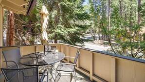 Een balkon met een ronde tafel en stoelen, met uitzicht op een bebost gebied met hoge bomen en een heldere lucht.