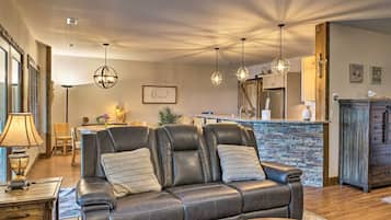 A living room with a leather sofa, dining area, kitchen with stone backsplash, and wooden ceiling beams.
