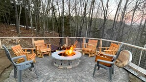 A circular outdoor seating area with a fire pit in the center, surrounded by wooden chairs and a metal railing. - Beaver Lake Retreat w/ Lake Access & Fire Pit! (Garfield)