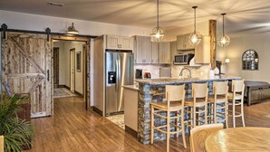 A spacious kitchen with a large island, bar stools, stainless steel appliances, and a rustic wooden door. - Beaver Lake Retreat w/ Lake Access & Fire Pit! (Garfield)