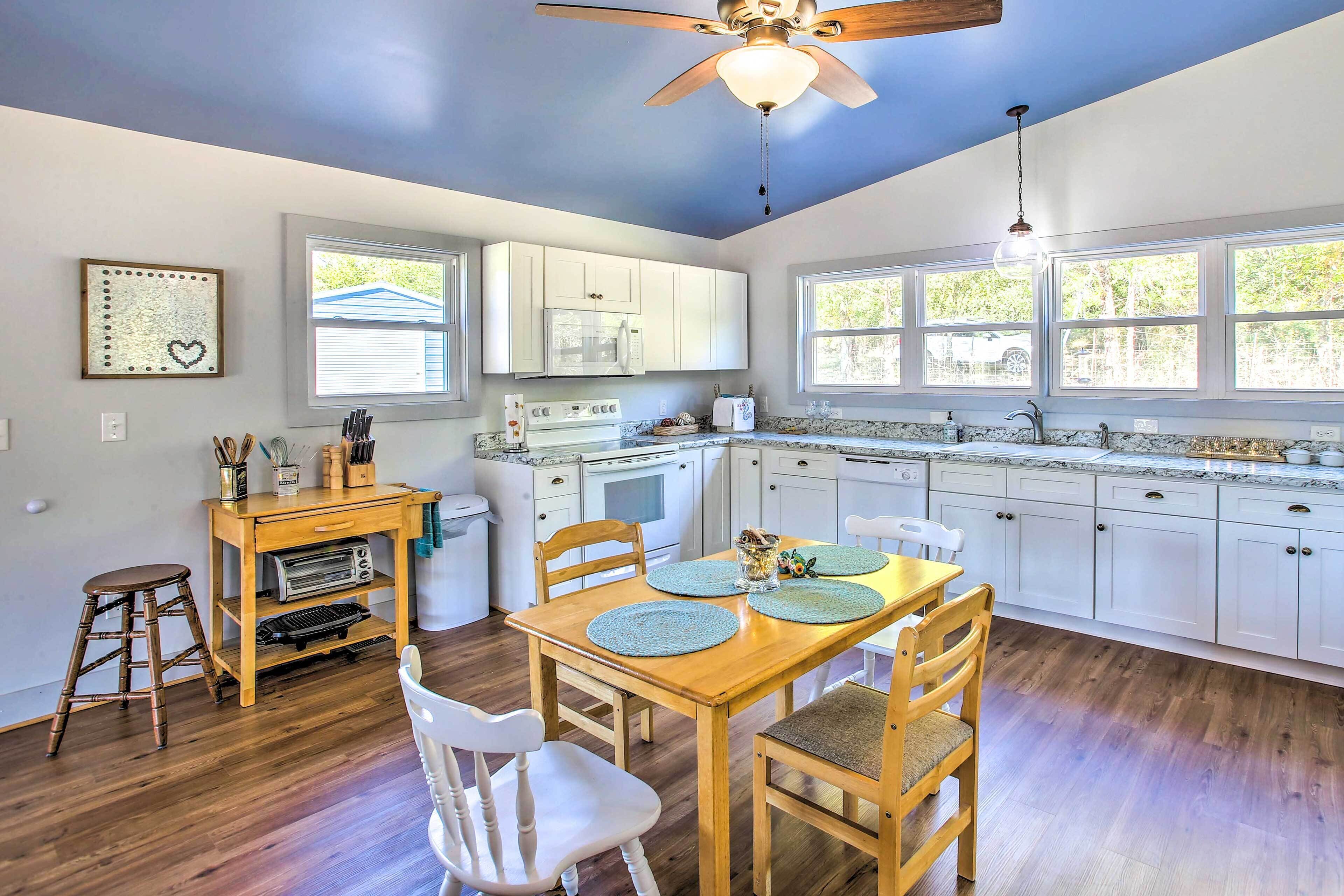 A kitchen with white cabinets, a wooden dining table with blue placemats, and a ceiling fan.