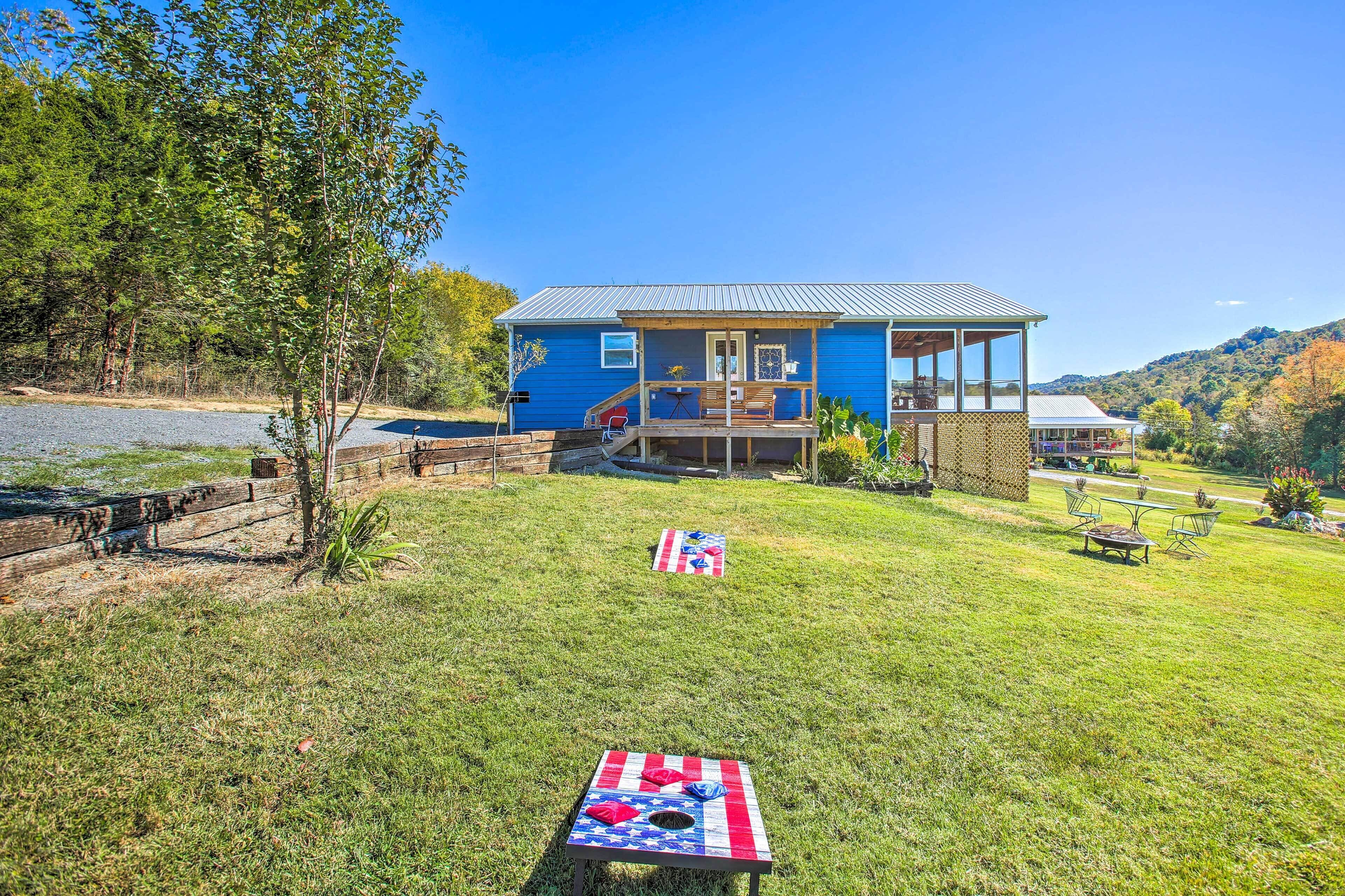 A blue house with a deck, a picnic table with a flag, and a grassy yard.