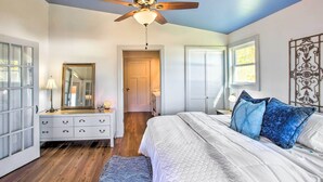 Un dormitorio con cama, cómoda, espejo, ventilador de techo y puerta que da a otra habitación.