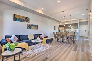 A modern living room with a dark blue sofa, a round coffee table, and a dining area with wooden chairs and a small table.