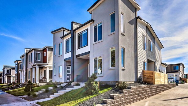 A modern multi-story residential building with a flat roof, large windows, and a well-maintained lawn.