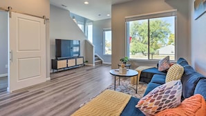 A modern living room with a staircase, a flat-screen TV, and a large window.