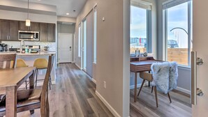 A modern kitchen with a built-in microwave and stainless steel appliances, a dining area with wooden furniture, and a view of the outside through large windows.