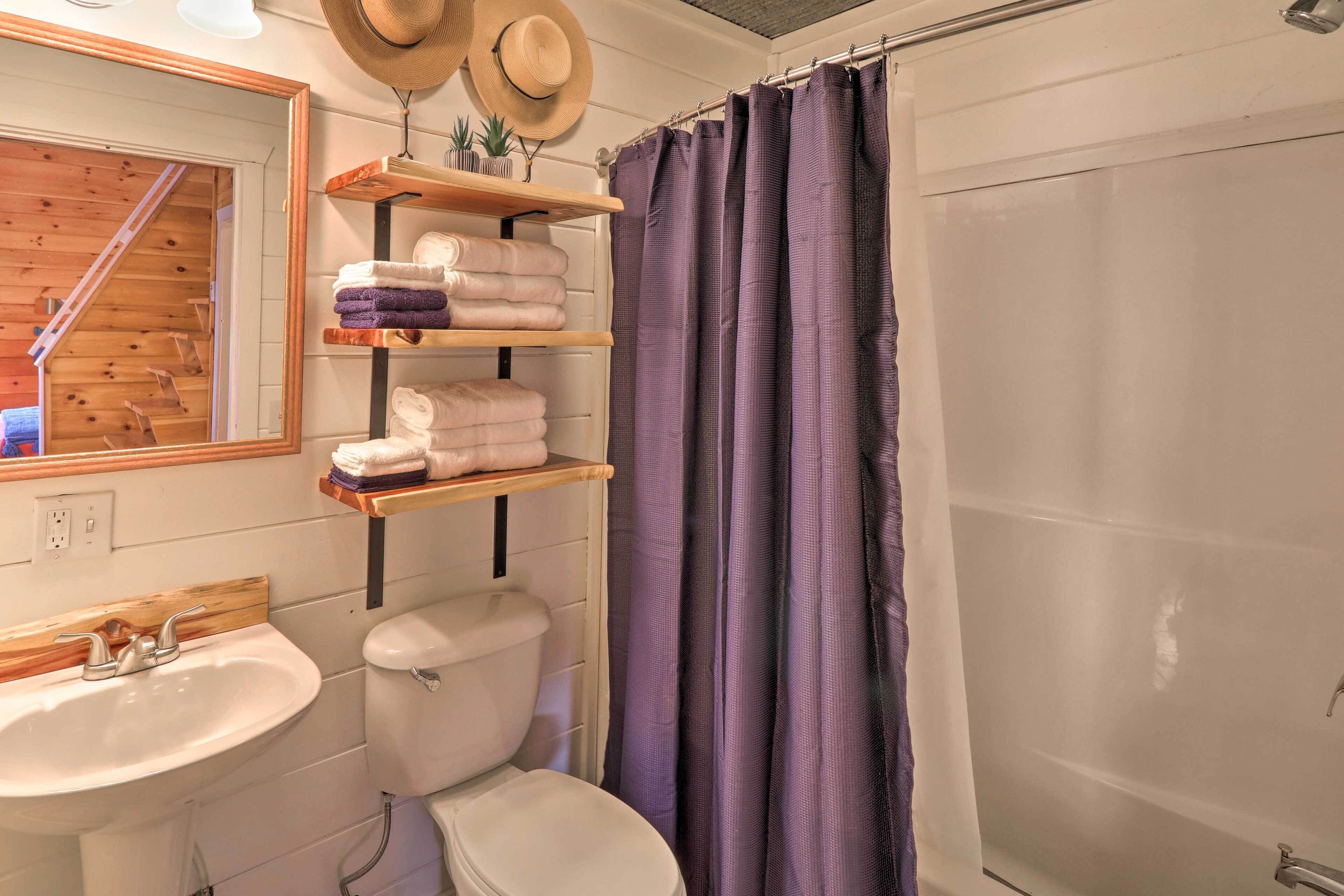 A bathroom with a wooden shelf holding towels, a white toilet, a sink, and a purple shower curtain.