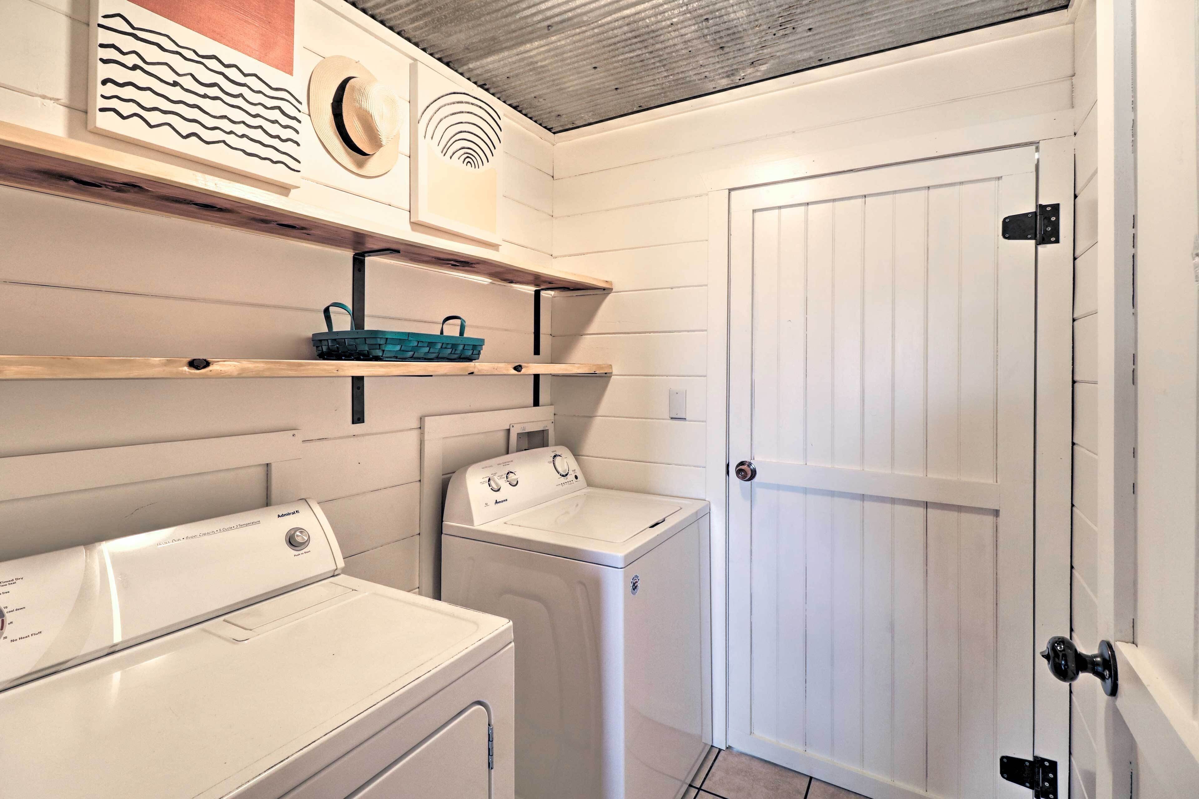 Un cuarto de lavandería con dos lavadoras, una secadora y estantes con una cesta y objetos decorativos.