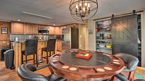 A modern kitchen with wooden cabinets, a central island, and a dining area with a round table and chairs. - Cozy Cabin With Sunroom & Cacapon River Access! (Capon Bridge)