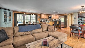 A spacious living room with a large brown sectional sofa, a wooden coffee table, and a dining area with a wooden table and chairs. - Cozy Cabin With Sunroom & Cacapon River Access! (Capon Bridge)