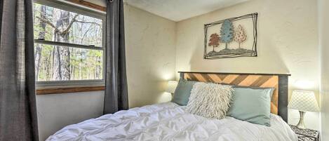 Un dormitorio con cama, ventana con cortinas, lámpara de pared y un cuadro enmarcado.
