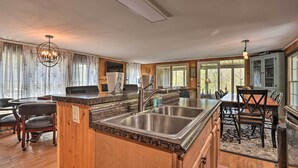 A spacious kitchen with a large island, wooden cabinetry, and a dining area with a chandelier. - Cozy Cabin With Sunroom & Cacapon River Access! (Capon Bridge)