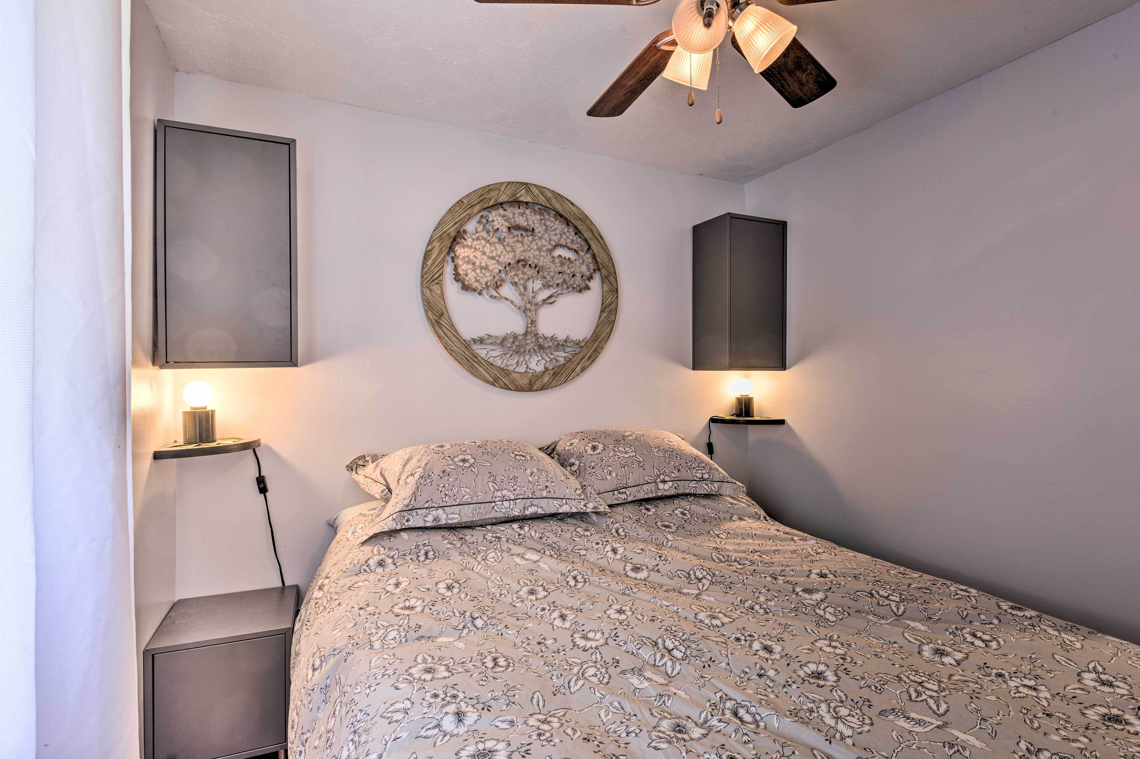 Une chambre à coucher avec un lit, une décoration murale en forme d’arbre, un ventilateur de plafond et deux lampes de chevet.