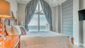 Un dormitorio con una cama grande, vistas al mar, un televisor en la pared y una mesita de noche de madera.