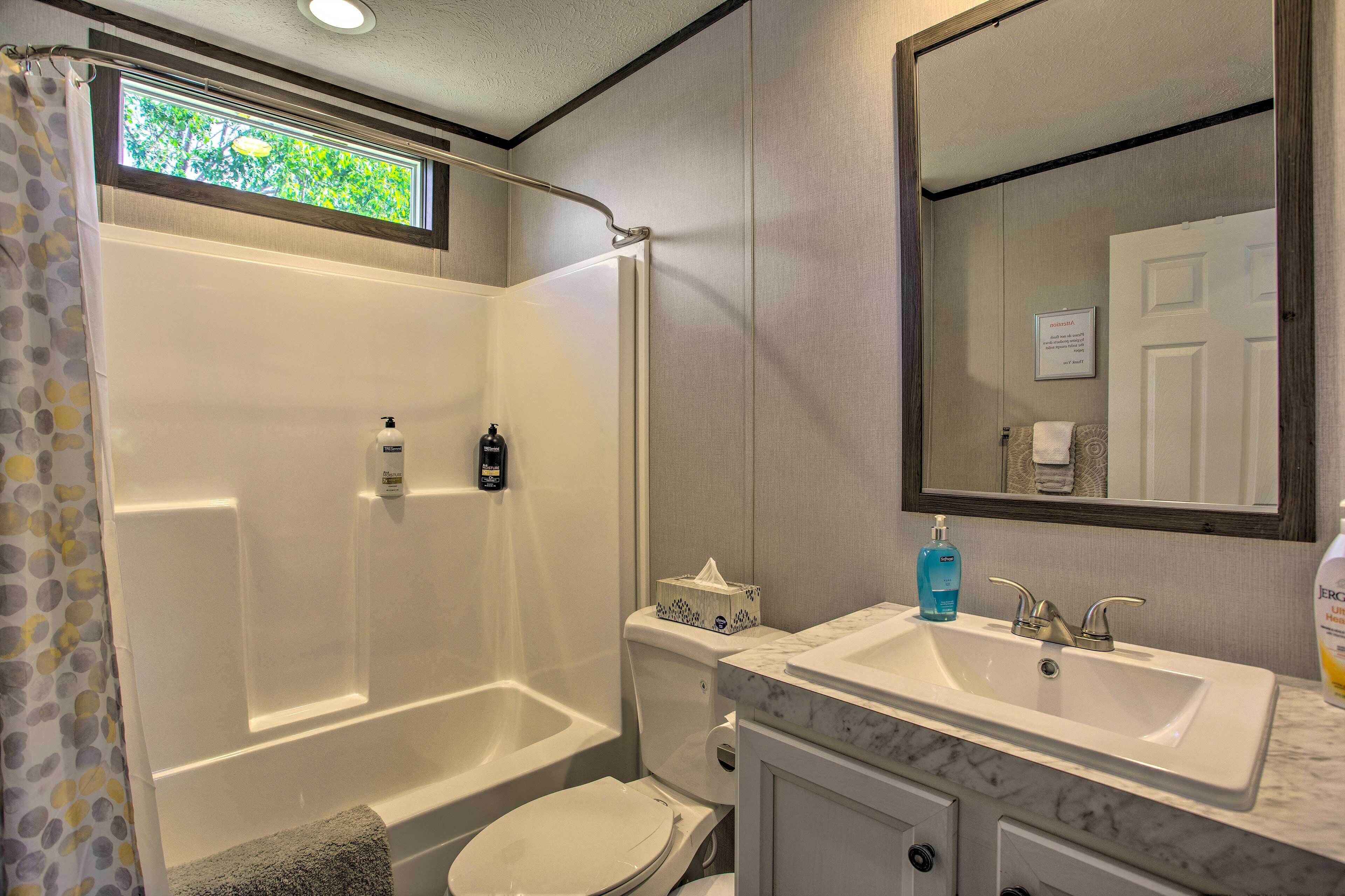 A bathroom with a shower, toilet, sink, and a large mirror.