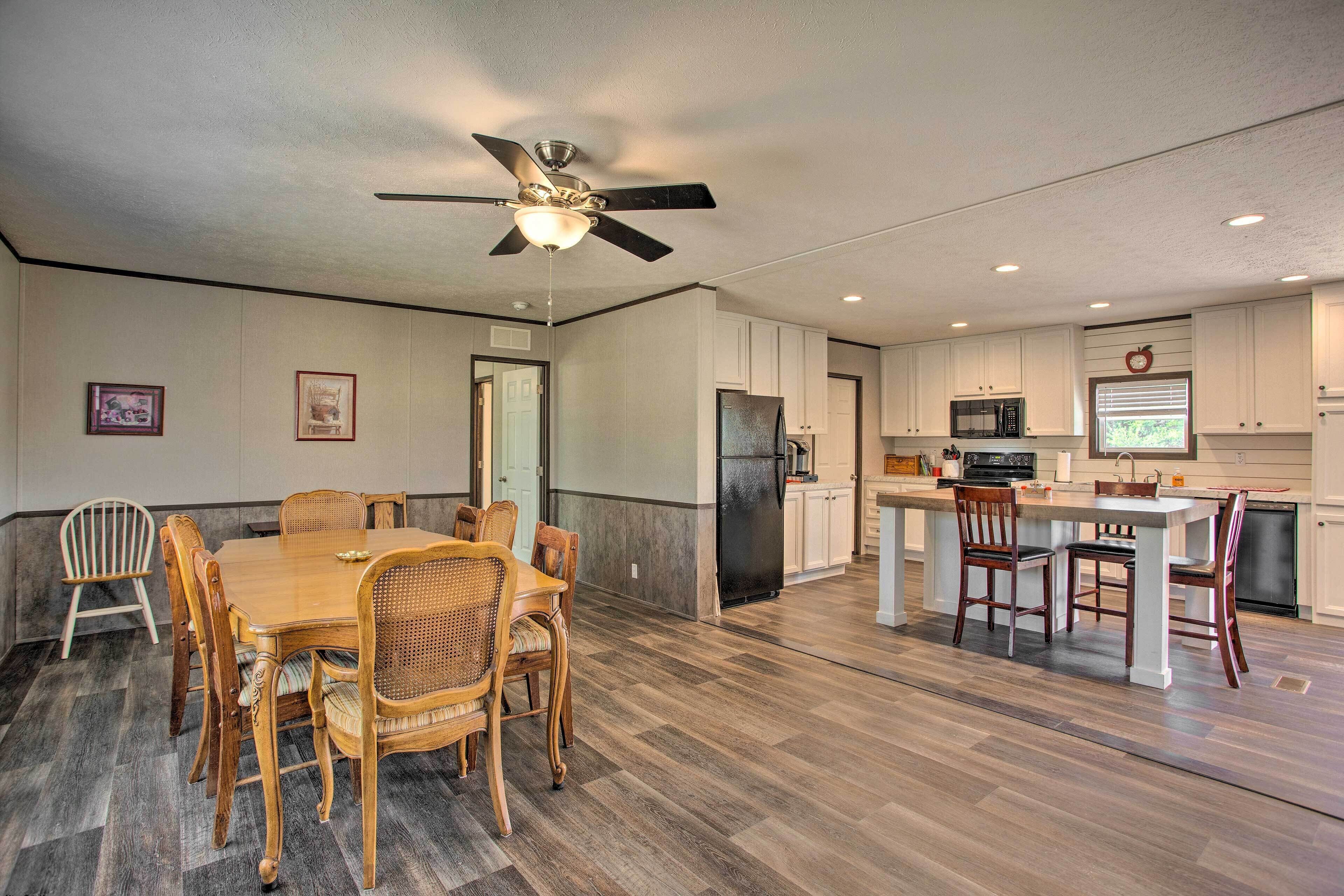 A spacious kitchen with a dining area, featuring a ceiling fan, wooden flooring, and white cabinetry.