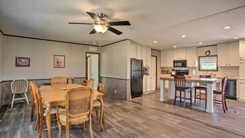 A spacious kitchen with a dining area, featuring a ceiling fan, wooden flooring, and white cabinetry.
