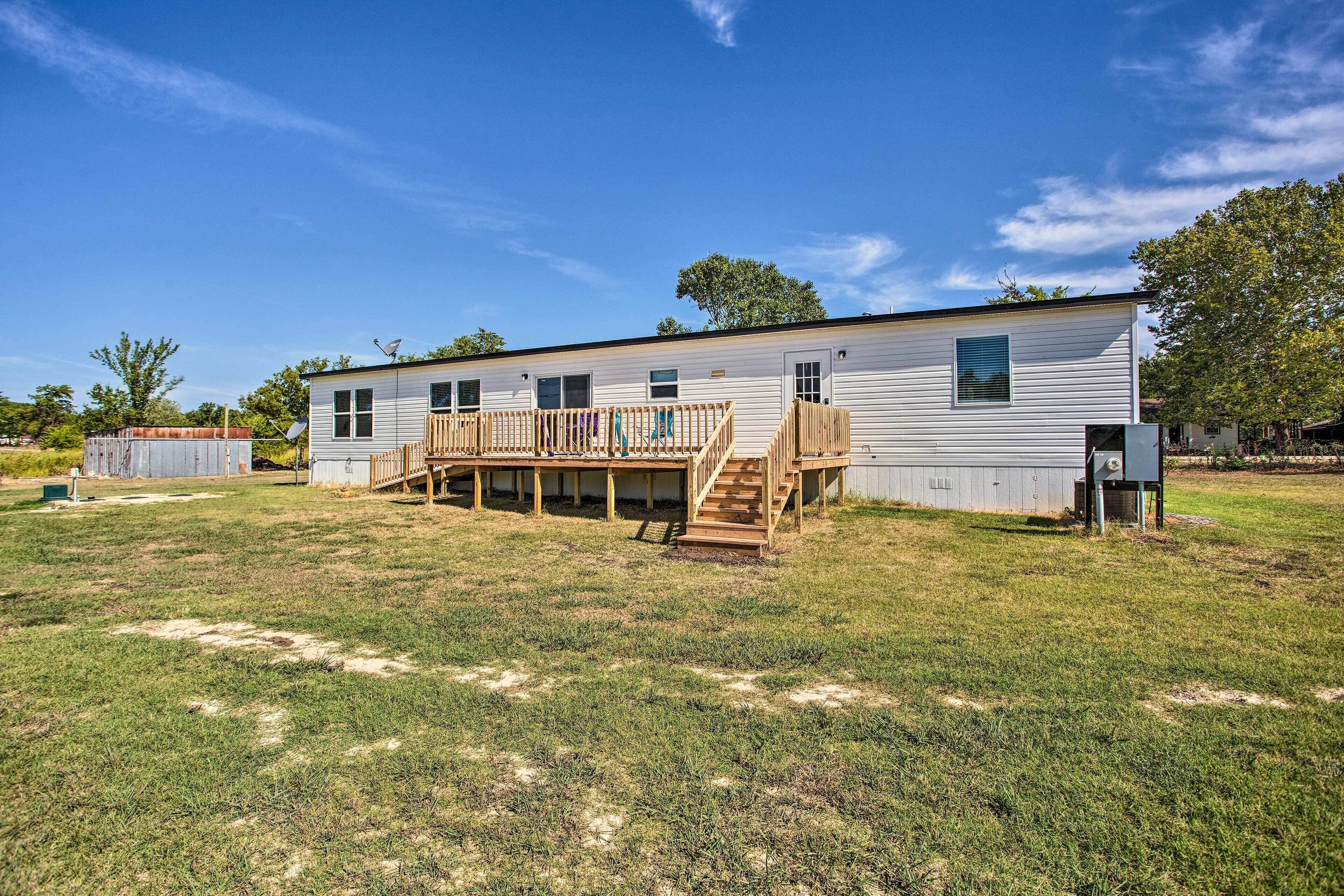 A single-story mobile home with a wooden deck and a staircase leading to a covered porch.