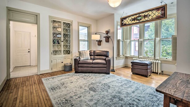 A spacious living room with a brown leather sofa, a patterned rug, a wooden coffee table, and a large window with shutters. - Spacious Getaway: 7 Mi to Whitetail Slopes! (Mercersburg)