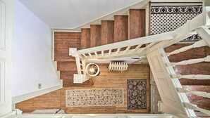 A staircase with wooden steps and white railings, leading to a landing with a patterned rug and a wall-mounted light fixture. - Spacious Getaway: 7 Mi to Whitetail Slopes! (Mercersburg)