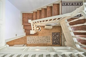 Una escalera con escalones de madera y barandillas blancas que conduce a un rellano con alfombra estampada y una lámpara fijada a la pared.