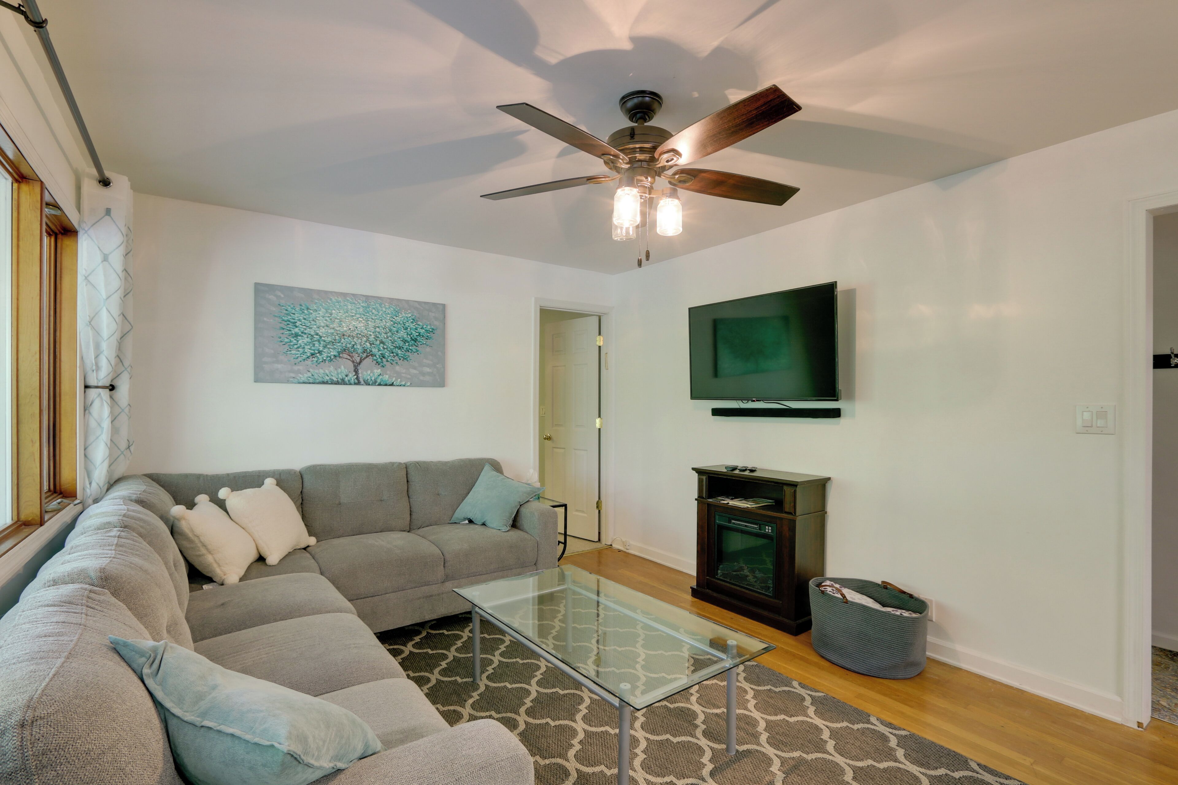 A living room with a sofa, a glass coffee table, a ceiling fan, a fireplace, and a television mounted on the wall.