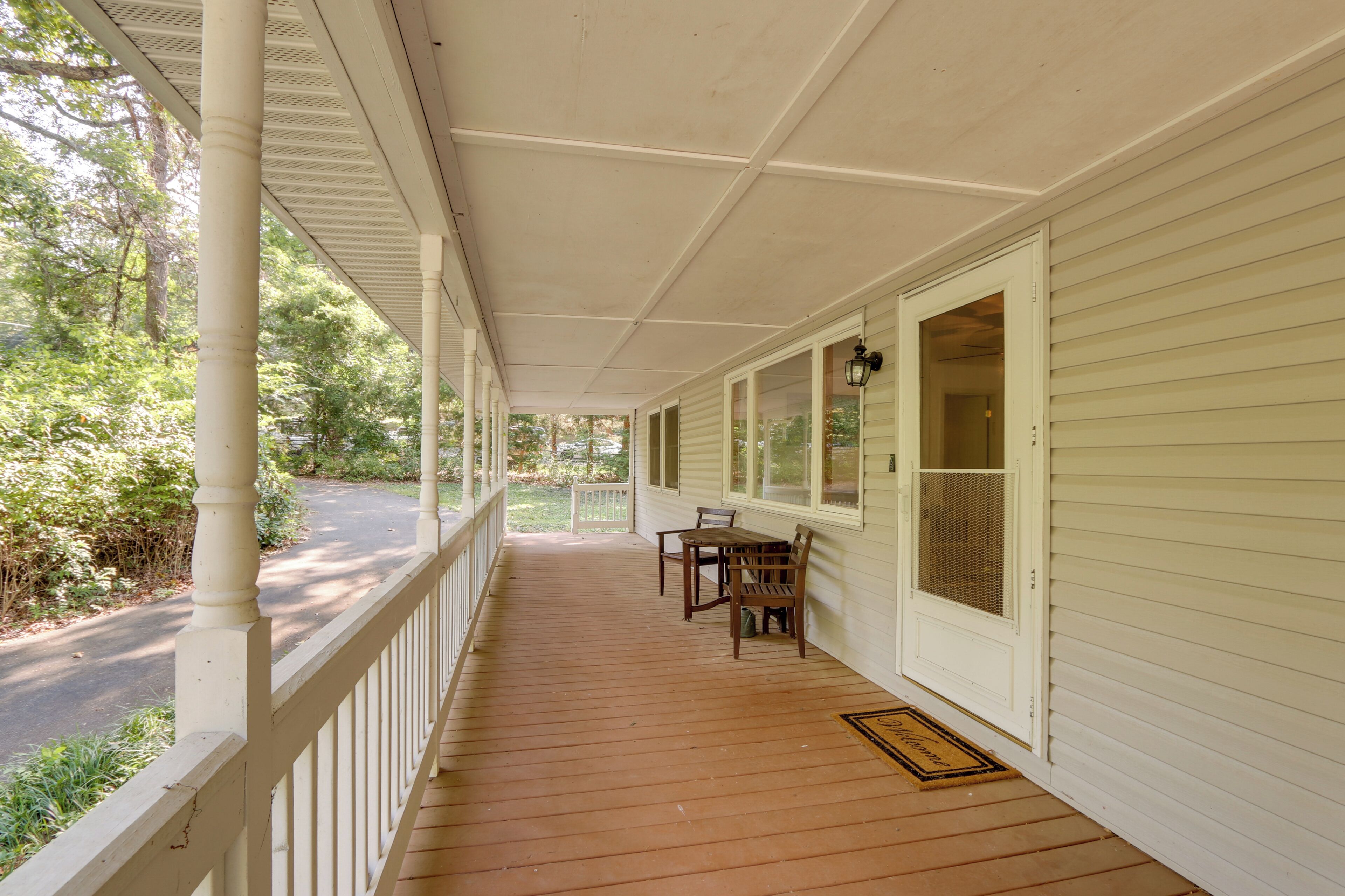 A covered porch with a wooden table and chairs, a door with a window, and a white railing.