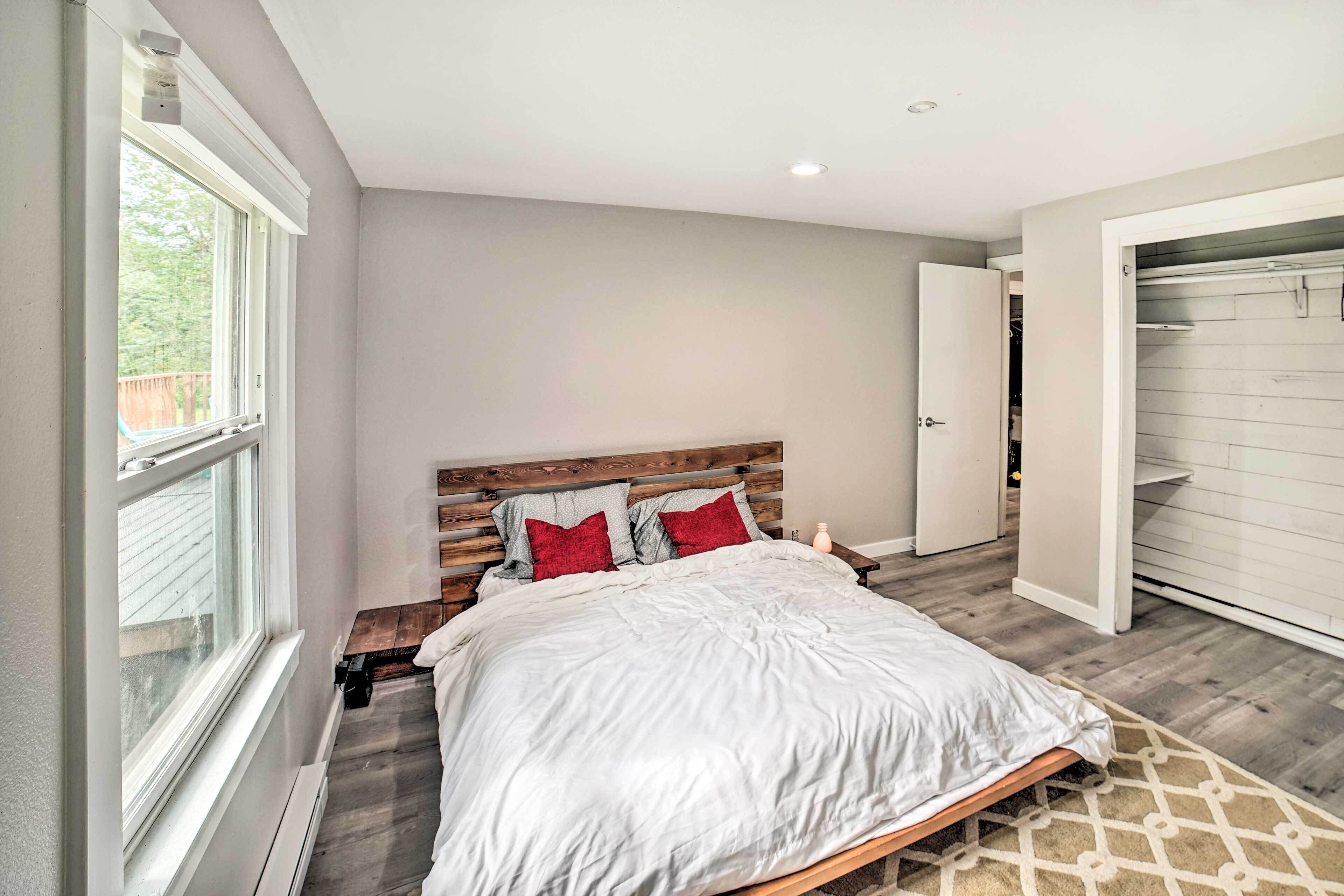 A bedroom with a wooden headboard, a large bed with white bedding, a window, and a closet with sliding doors.