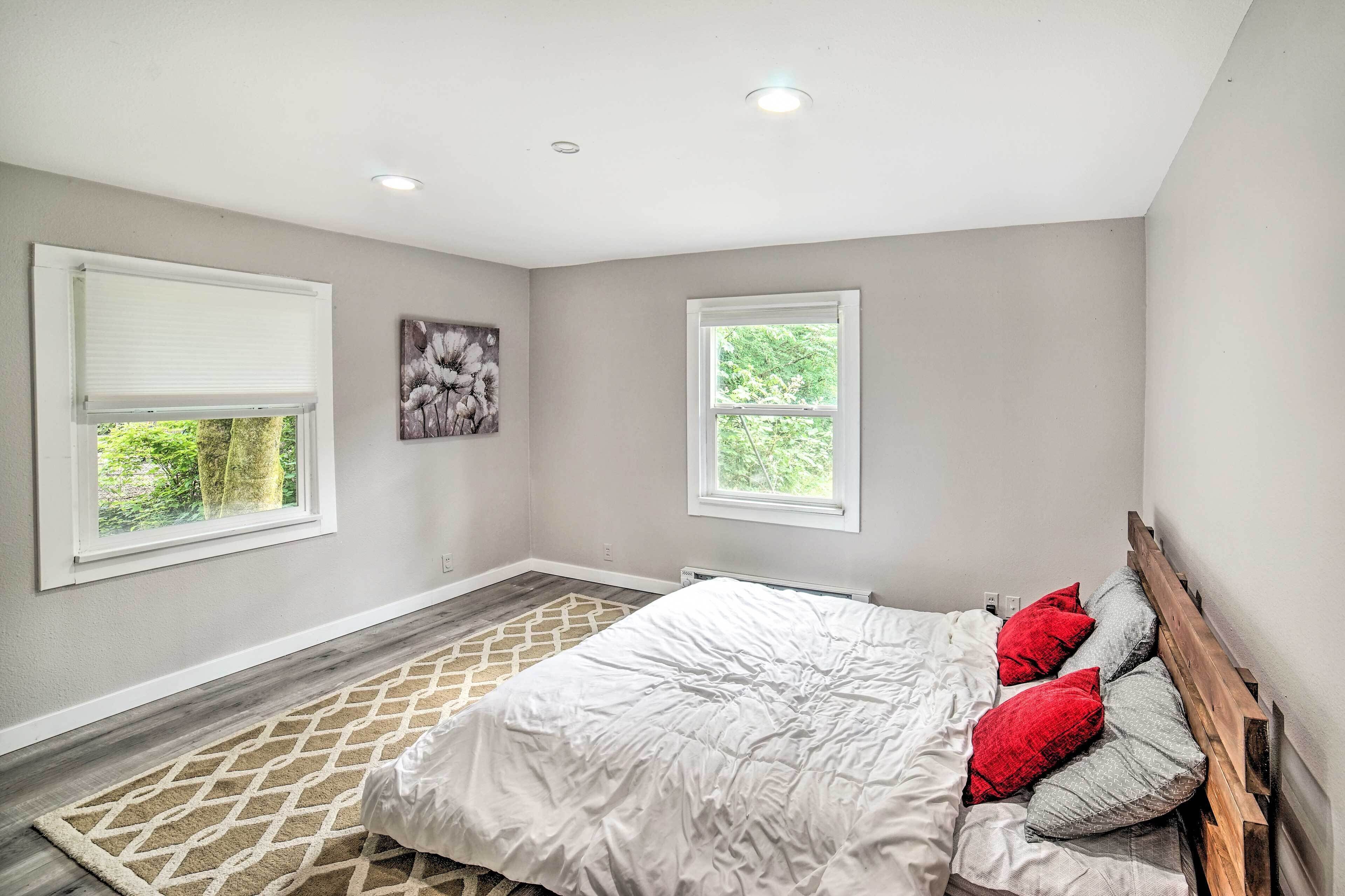 A bedroom with a bed, two windows, a radiator, and a wall-mounted artwork.