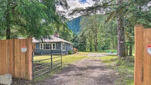 A rustic cabin with a wooden gate, surrounded by dense forest and mountains.