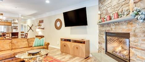 Una sala de estar con chimenea de piedra, un televisor de pantalla plana, un mueble de madera y un tapete rojo estampado.
