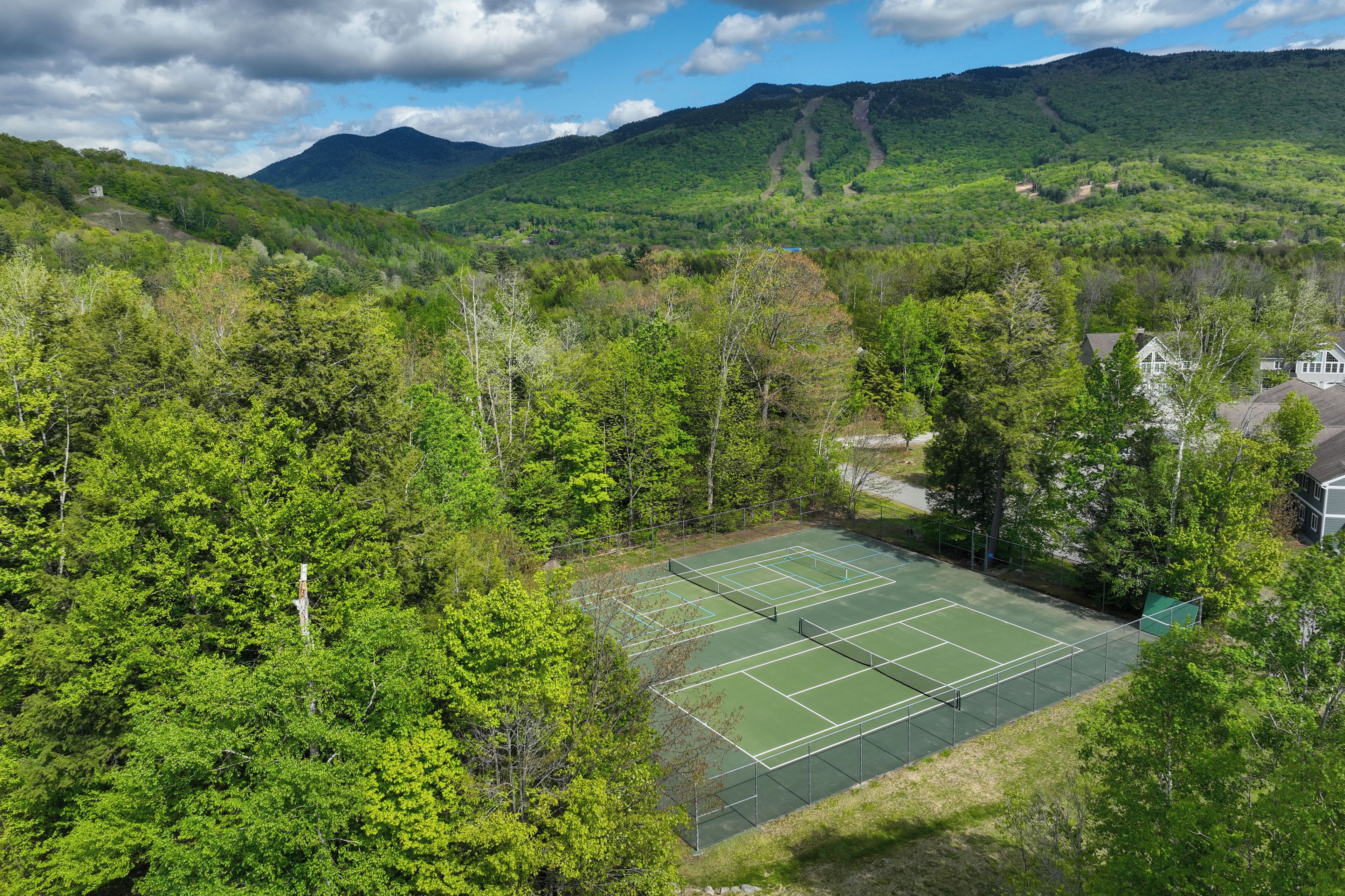 Una cancha de tenis rodeada de bosque denso y montañas.